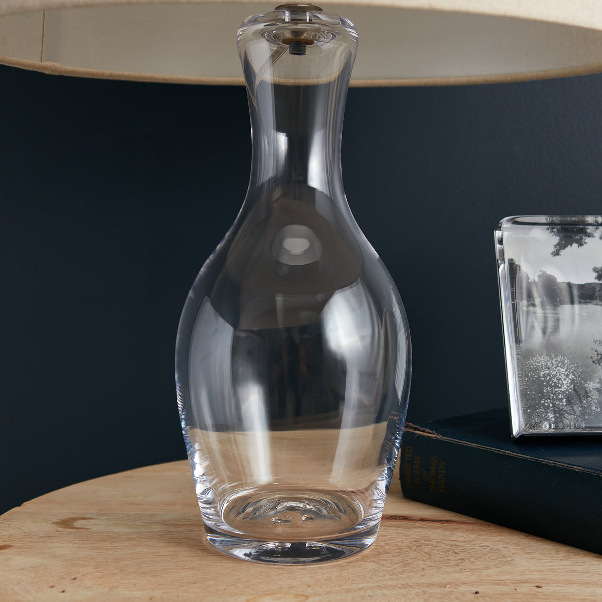 Clear glass table lamp with curved bottle shape and metal top on wooden surface.