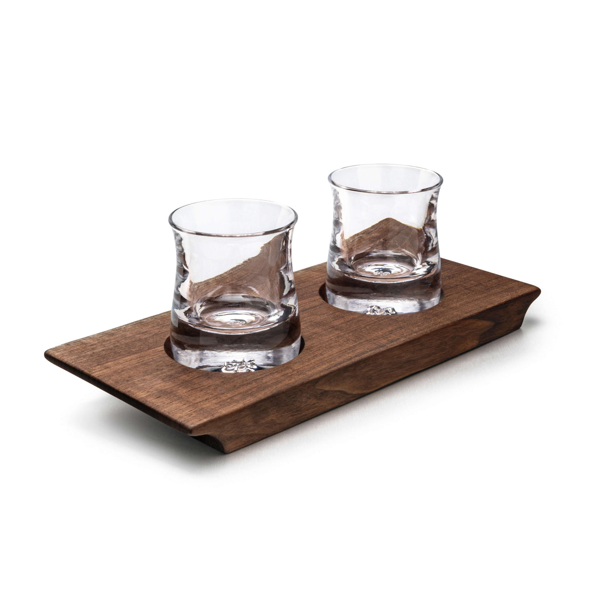 Two clear glass whiskey glasses with etched design on walnut wood serving base.