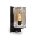 Black metal wall sconce with clear seeded glass cylinder shade and lit filament bulb inside.