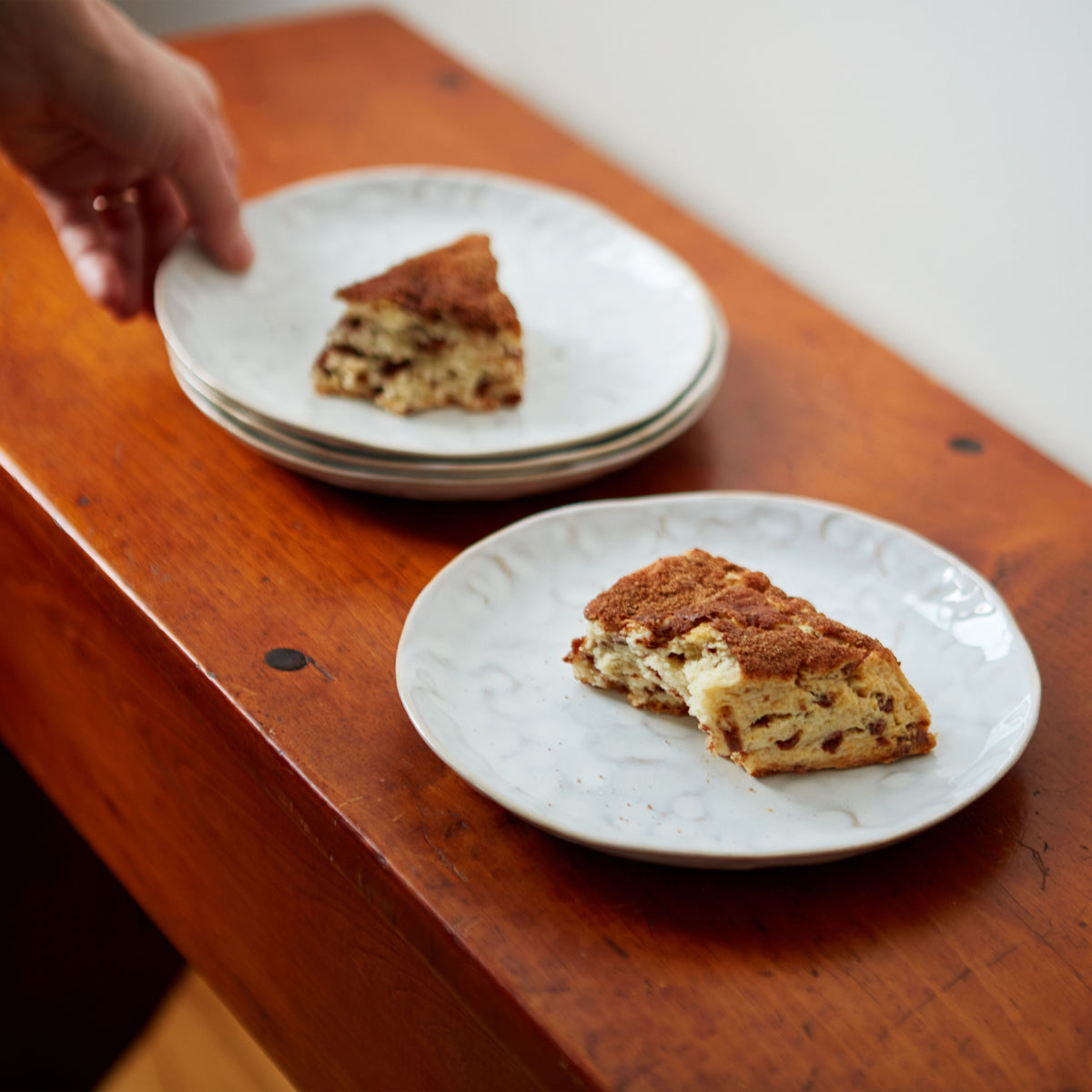 Set of four white appetizer plates with subtle cloud pattern, each holding cake slices on wooden surface.