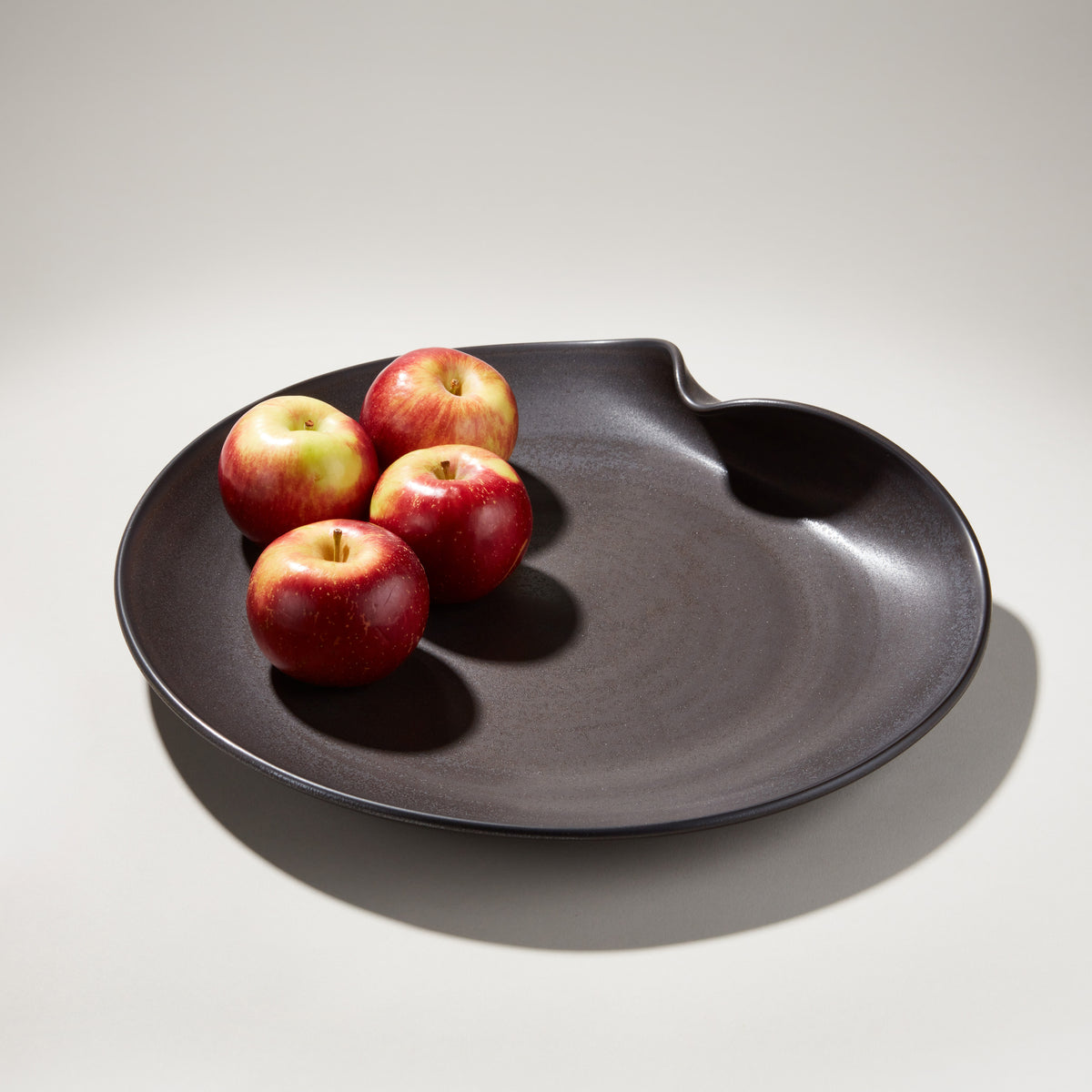 Black organic platter with wavy edges holding four red apples.