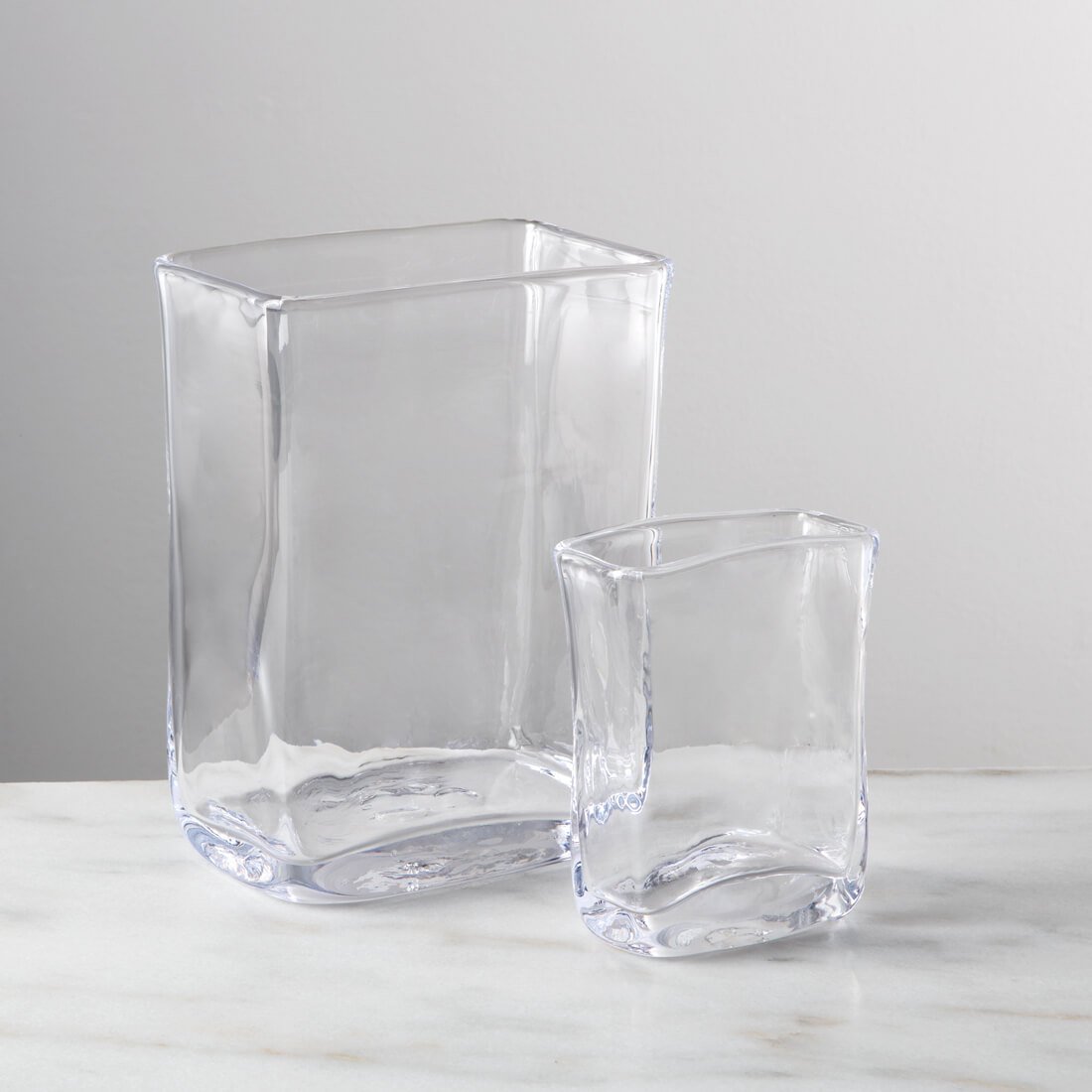 Two clear glass rectangular vases in different sizes with curved sides and rounded bases.