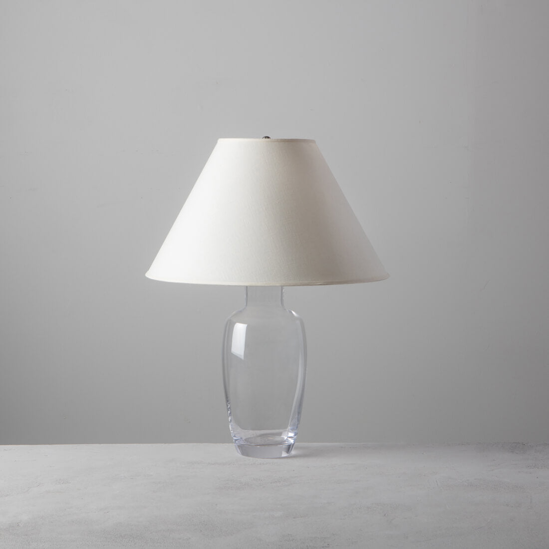 Tall lamp with clear glass base and white conical shade.
