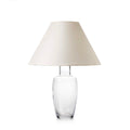 Tall table lamp with clear glass barrel-shaped base and cream-colored linen shade.