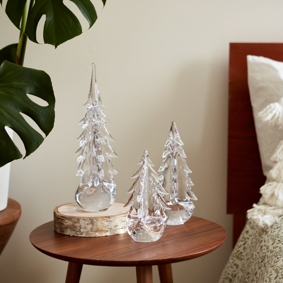 Three clear glass evergreen trees on a wooden table, with the tallest positioned on a birch wood round base.