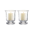 Pair of clear glass hurricane candleholders with cream pillar candles and lit wicks.