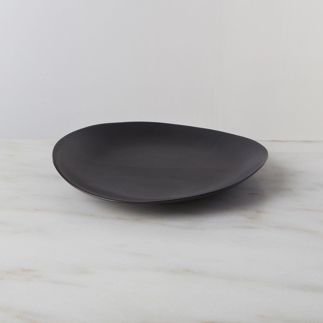 Slate-colored oval dinner plate with curved sides on a marble surface.