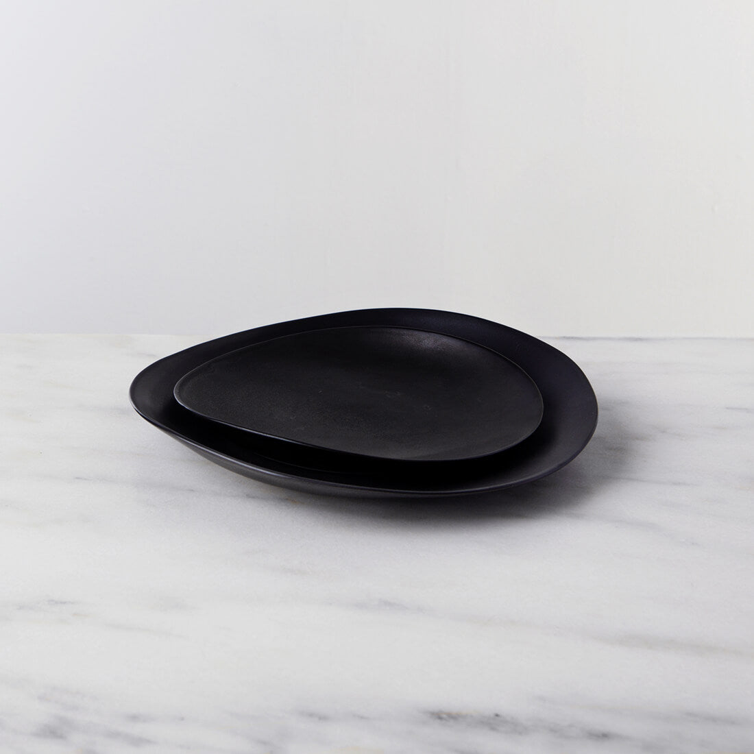 Two dark slate dinnerplates stacked together on a marble surface.