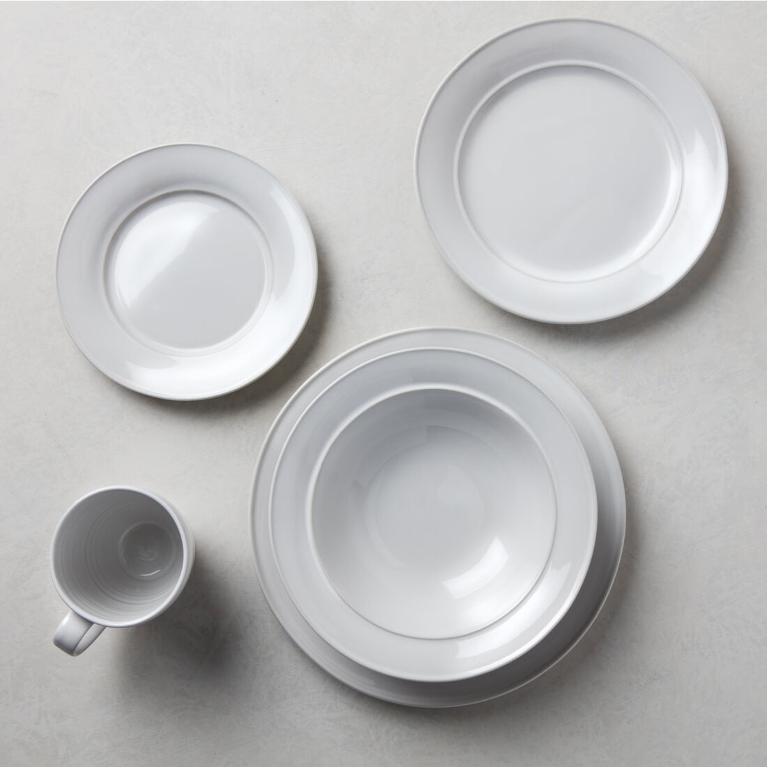 White dinnerware set including two plates, a bowl, and a mug with concentric ring detail.