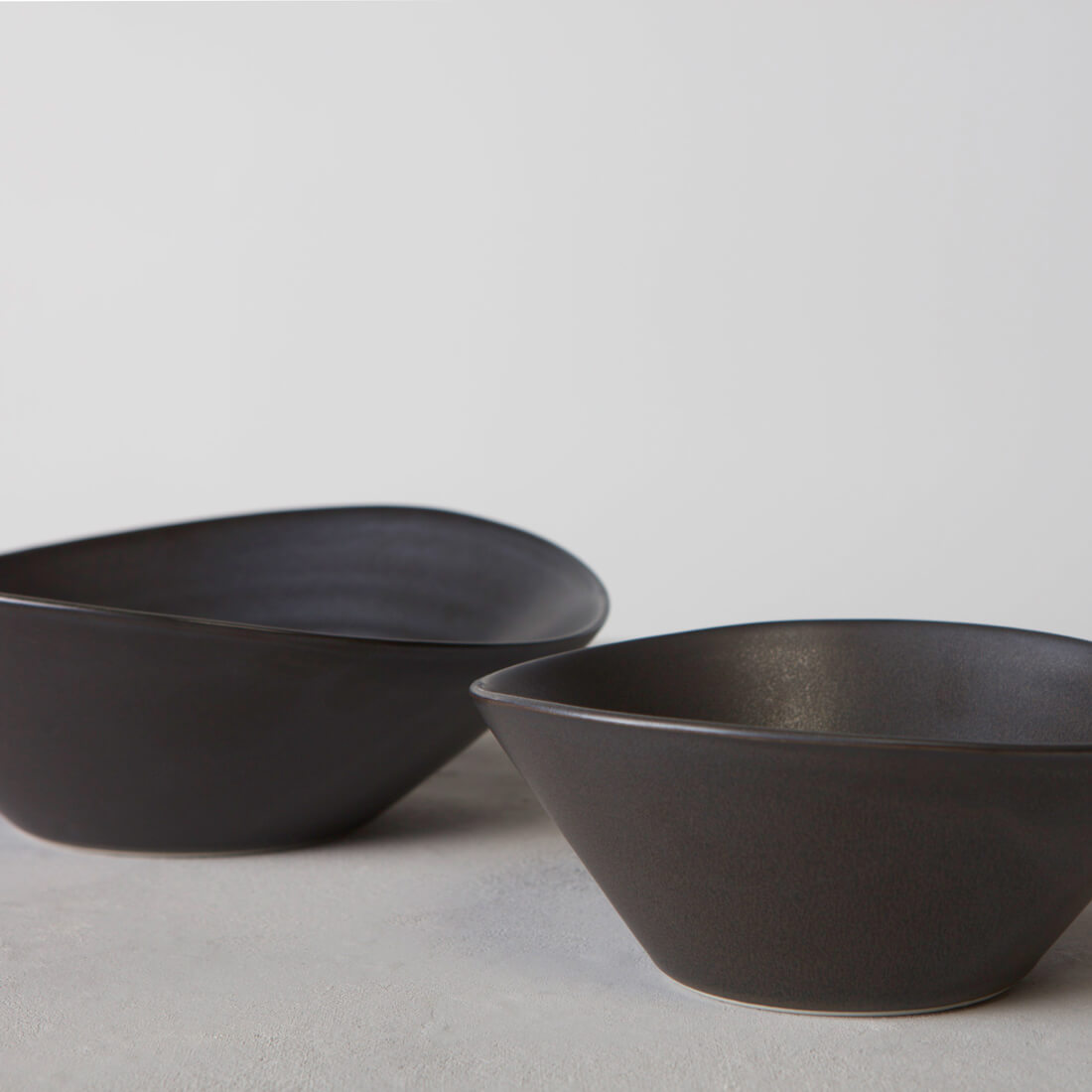 Two slate-colored ceramic bowls with curved rims and matte finish displayed on a neutral surface.