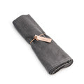 Grey linen table runner rolled and tied with a rose gold band.