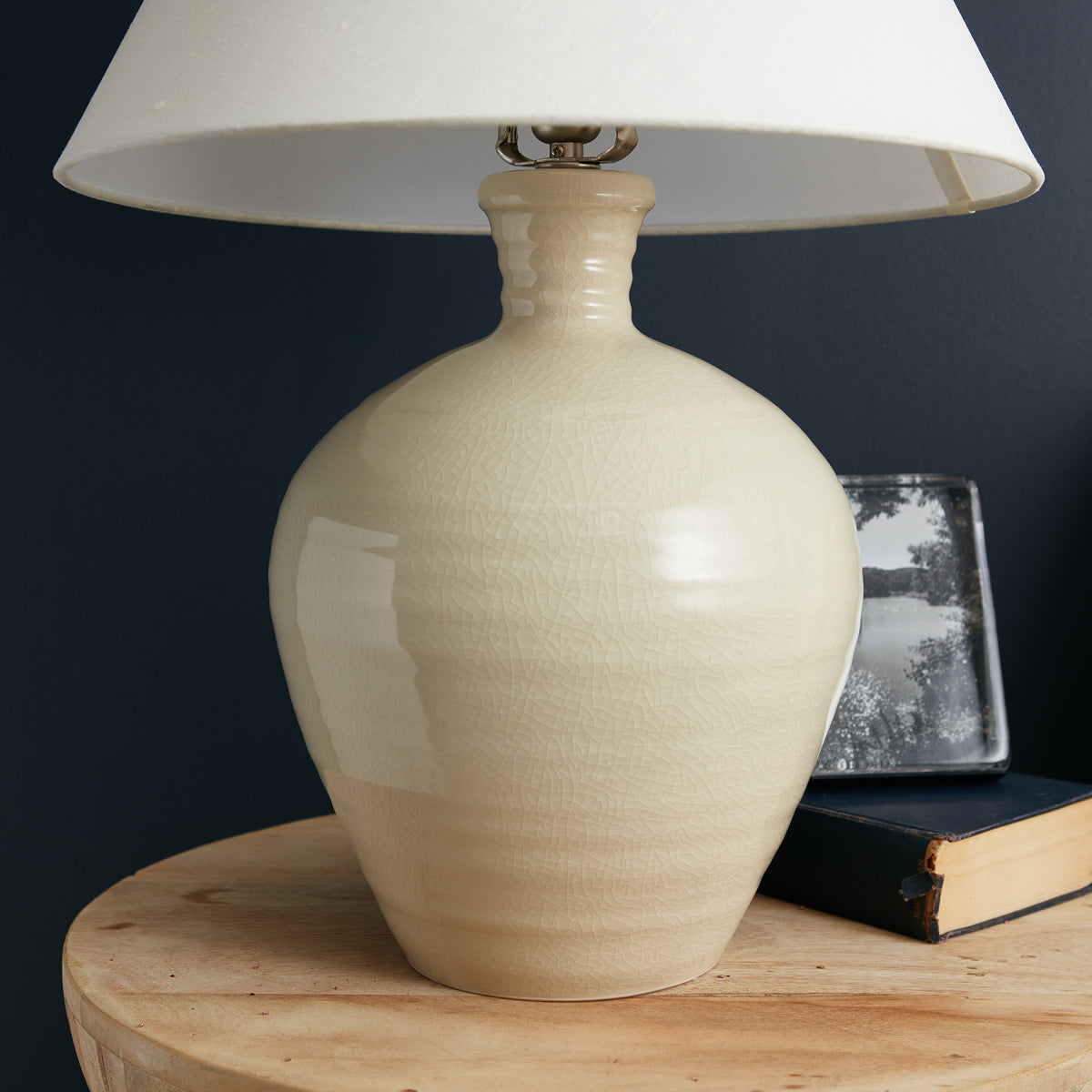Cream ceramic lamp with rounded bulbous base, brass hardware, and white linen shade.