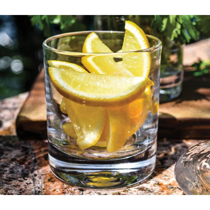 Rocks glass with gold rim containing amber liquid and lemon slices, set on stone surface outdoors.