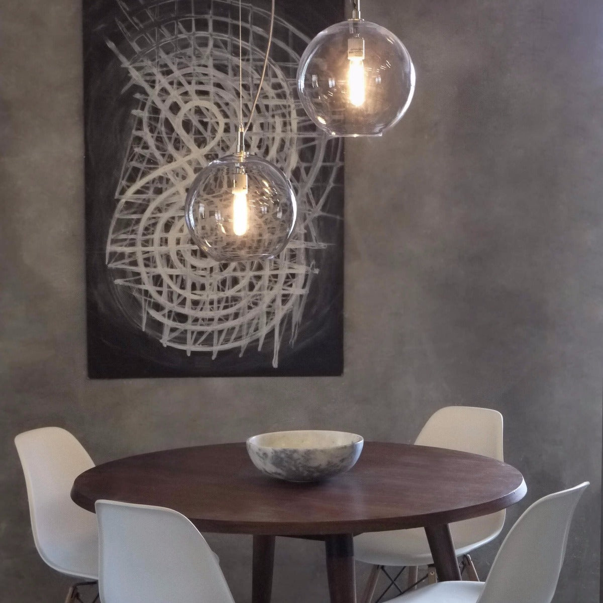 Two clear glass spherical pendants with glowing bulbs suspended above a dining table.