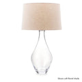 Clear glass teardrop-shaped table lamp base with beige linen drum shade.