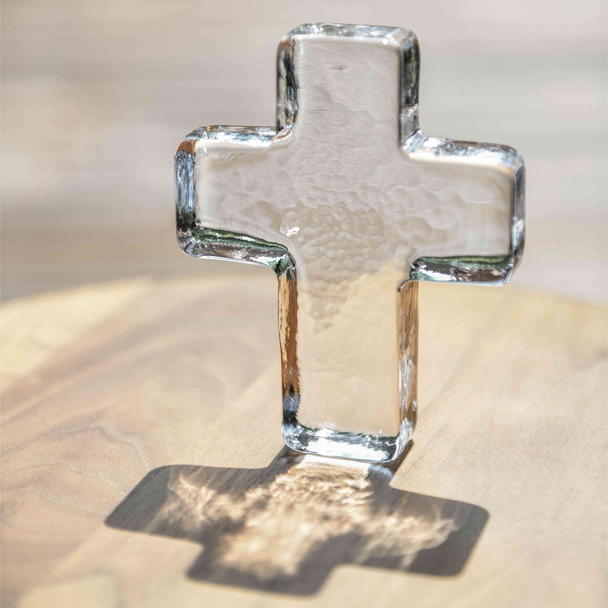 Clear glass cross with textured surface and beveled edges on a light wood background.
