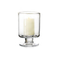 Clear glass hurricane vase with pedestal base containing a cream-colored pillar candle.