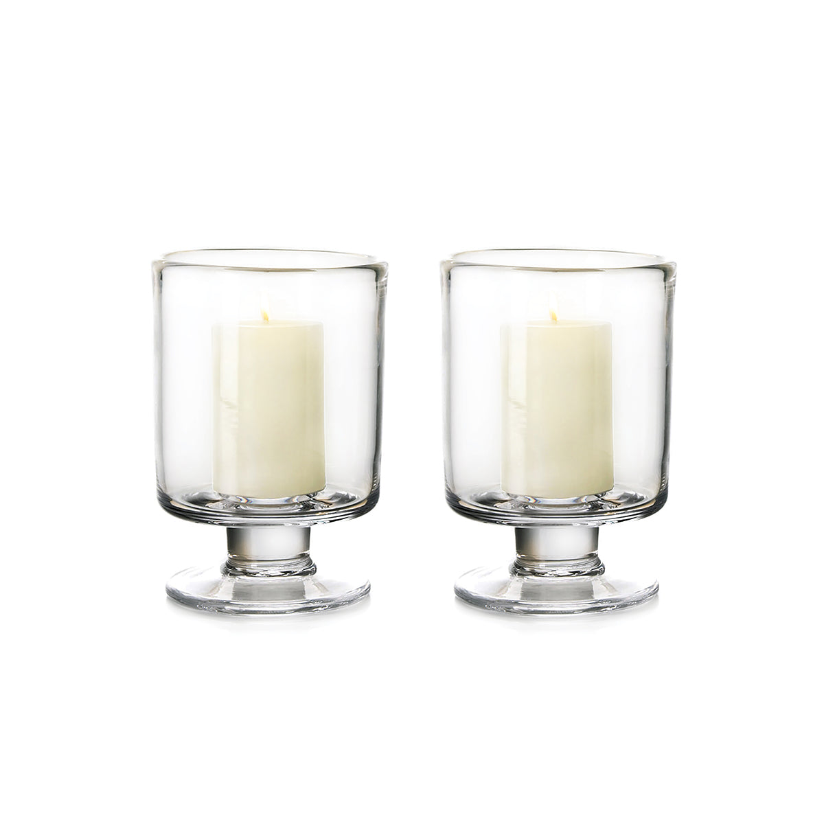 Two clear glass hurricane candle holders with pedestal bases, each containing a cream-colored pillar candle.