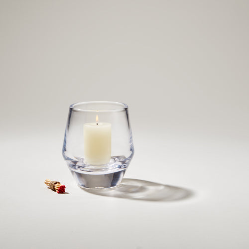 Clear glass votive holder with lit cream-colored candle inside and matches beside it.