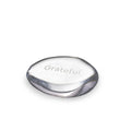 Clear glass stone with "Grateful" engraved on top surface and dark gray curved edges.