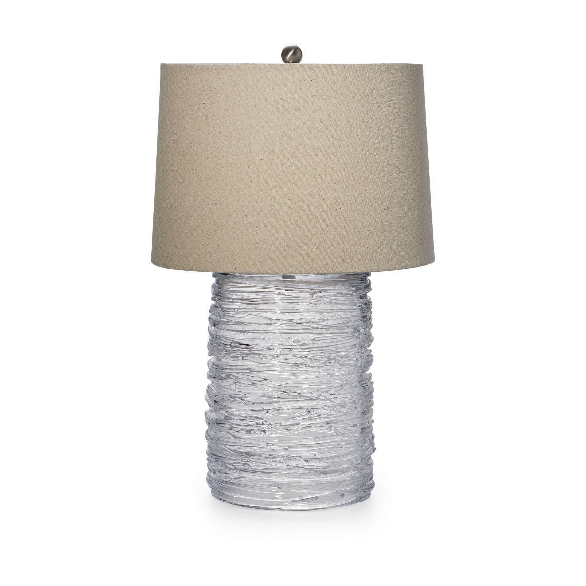 Table lamp with textured clear glass cylindrical base and wide beige linen shade with brushed metal finial.