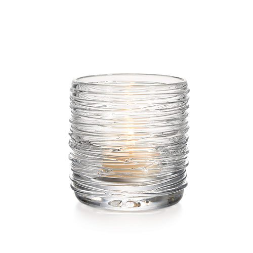 Clear glass tealight holder with horizontal ridged texture and lit candle inside.