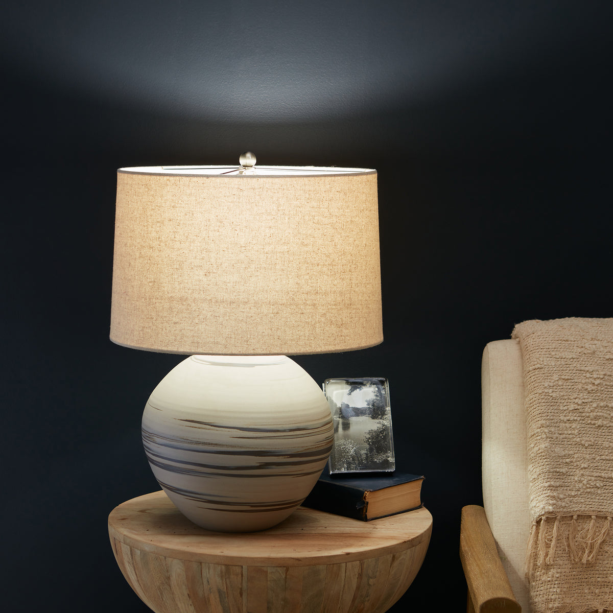 Round ceramic lamp base with horizontal stripe pattern and linen shade on wooden table.