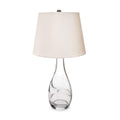 Table lamp with clear glass teardrop base, narrow neck, and cream linen shade with metal finial.