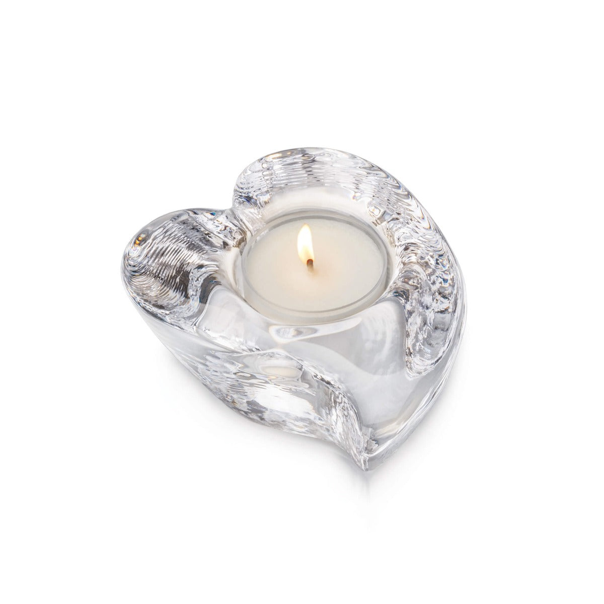 Clear glass heart-shaped tealight holder with lit cream candle inside.