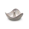 Cream-colored ceramic ring holder with wavy edges and a central cone post, featuring subtle etched details.