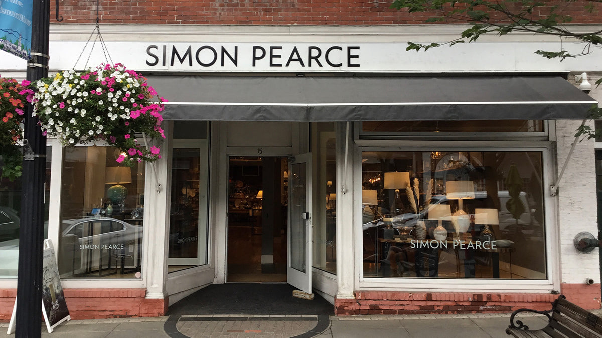 Exterior of the Simon Pearce retail store at 15 South Main Street in Hanover, New Hampshire, a brick storefront with a gray awning and hanging flower baskets