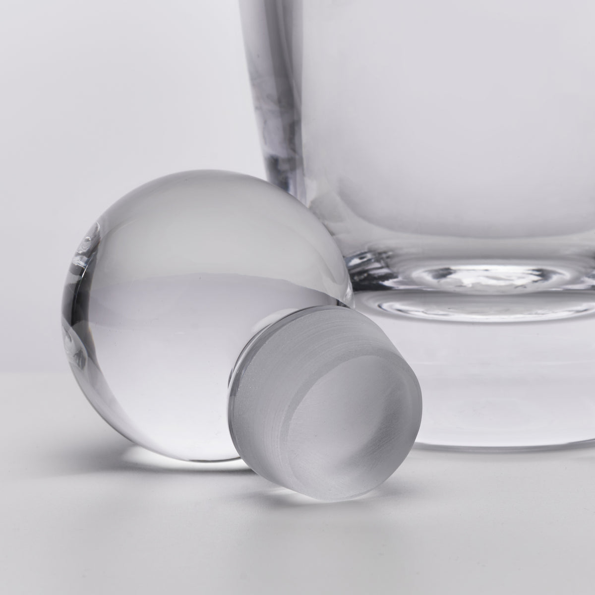 Clear glass decanter with spherical stopper and matching round ice ball, shown against white background.