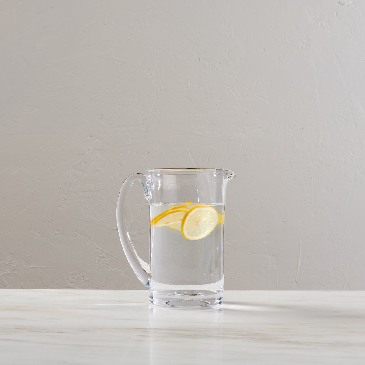 Clear glass pitcher filled with water and lemon slices on a white surface.