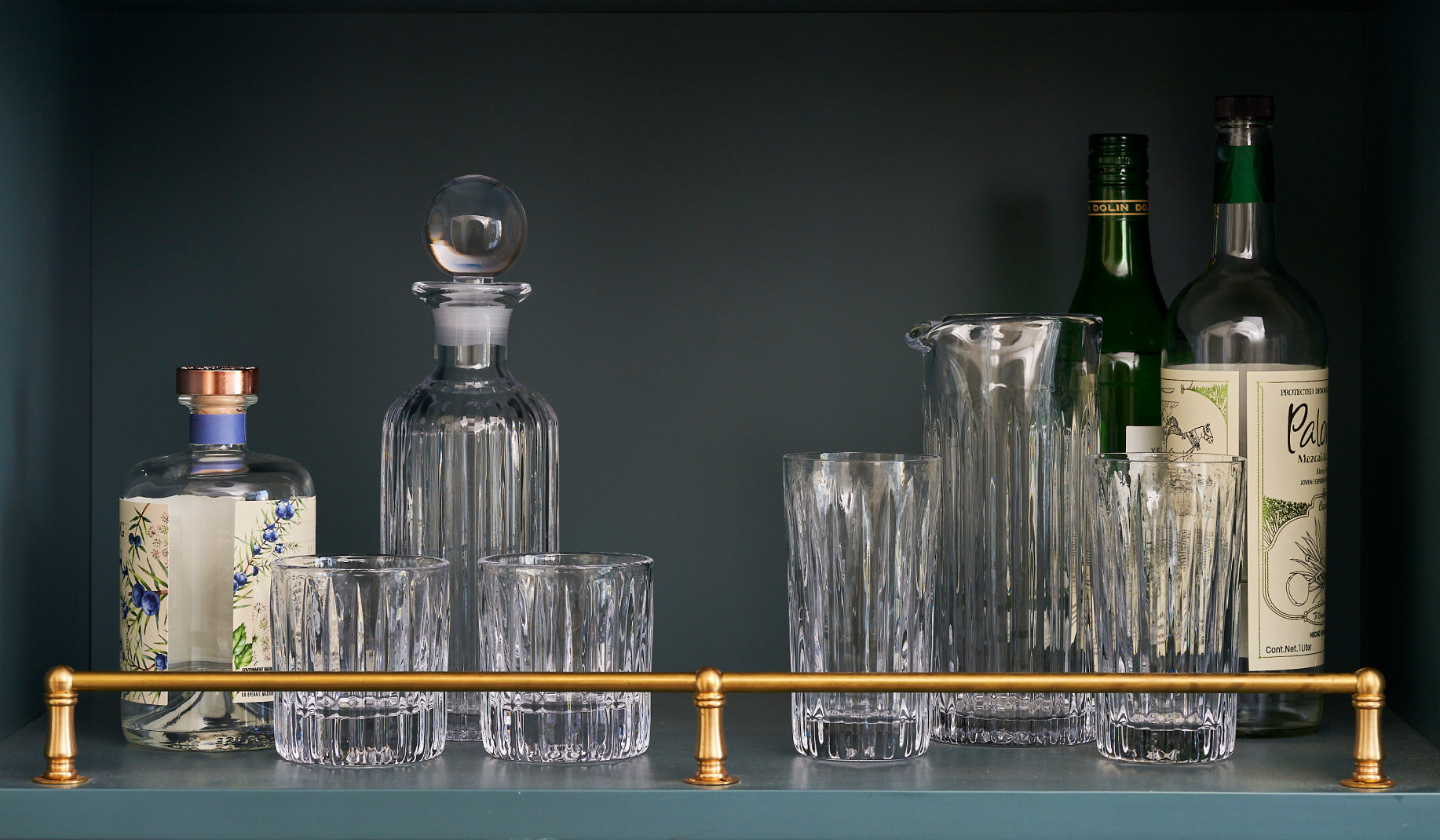 Simon Pearce Montpelier barware collection including a faceted decanter, double old fashioned glasses, highball glasses, and a mixing pitcher styled on a dark bar shelf with spirit bottles