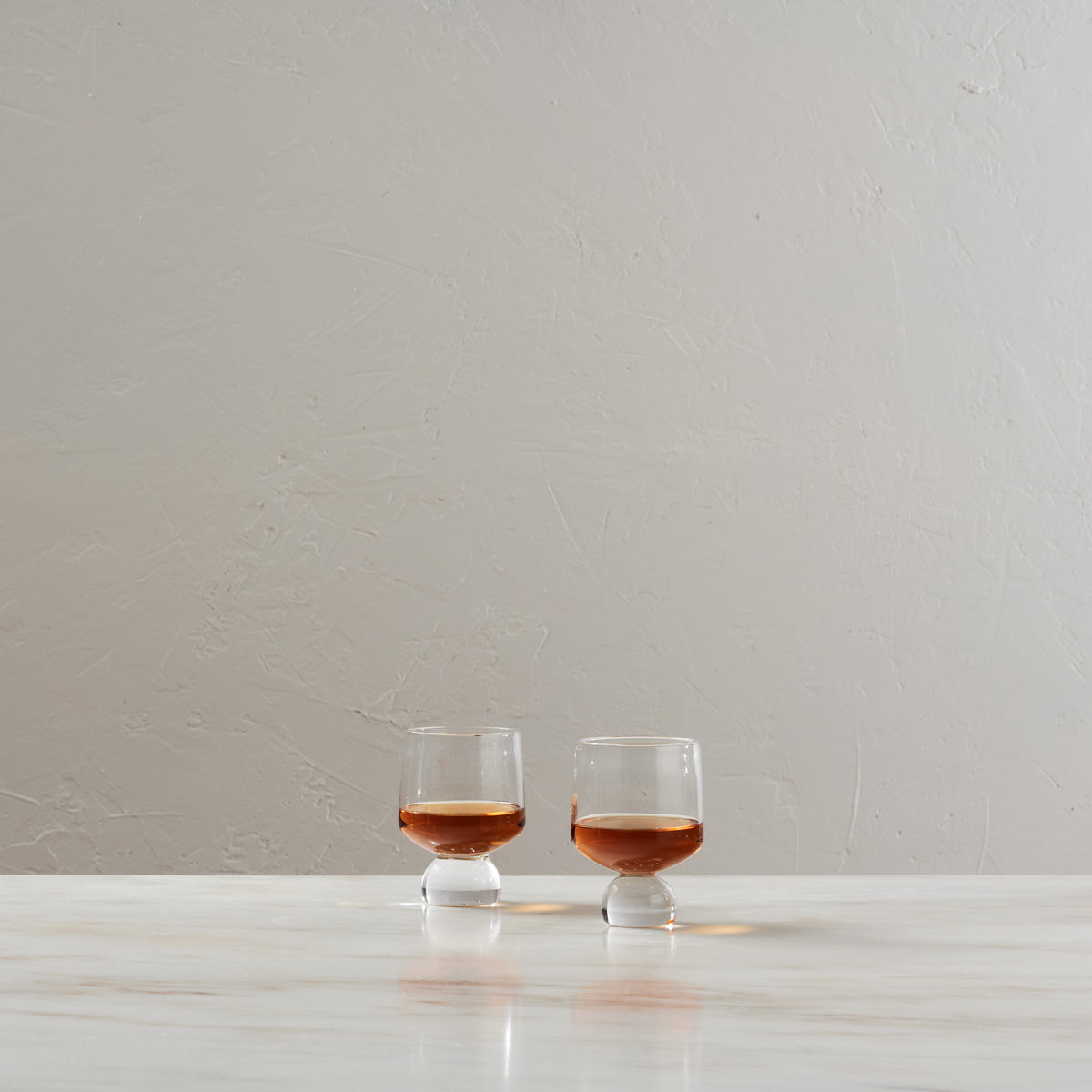 Two glasses filled with bourbon on a white surface against a neutral background.