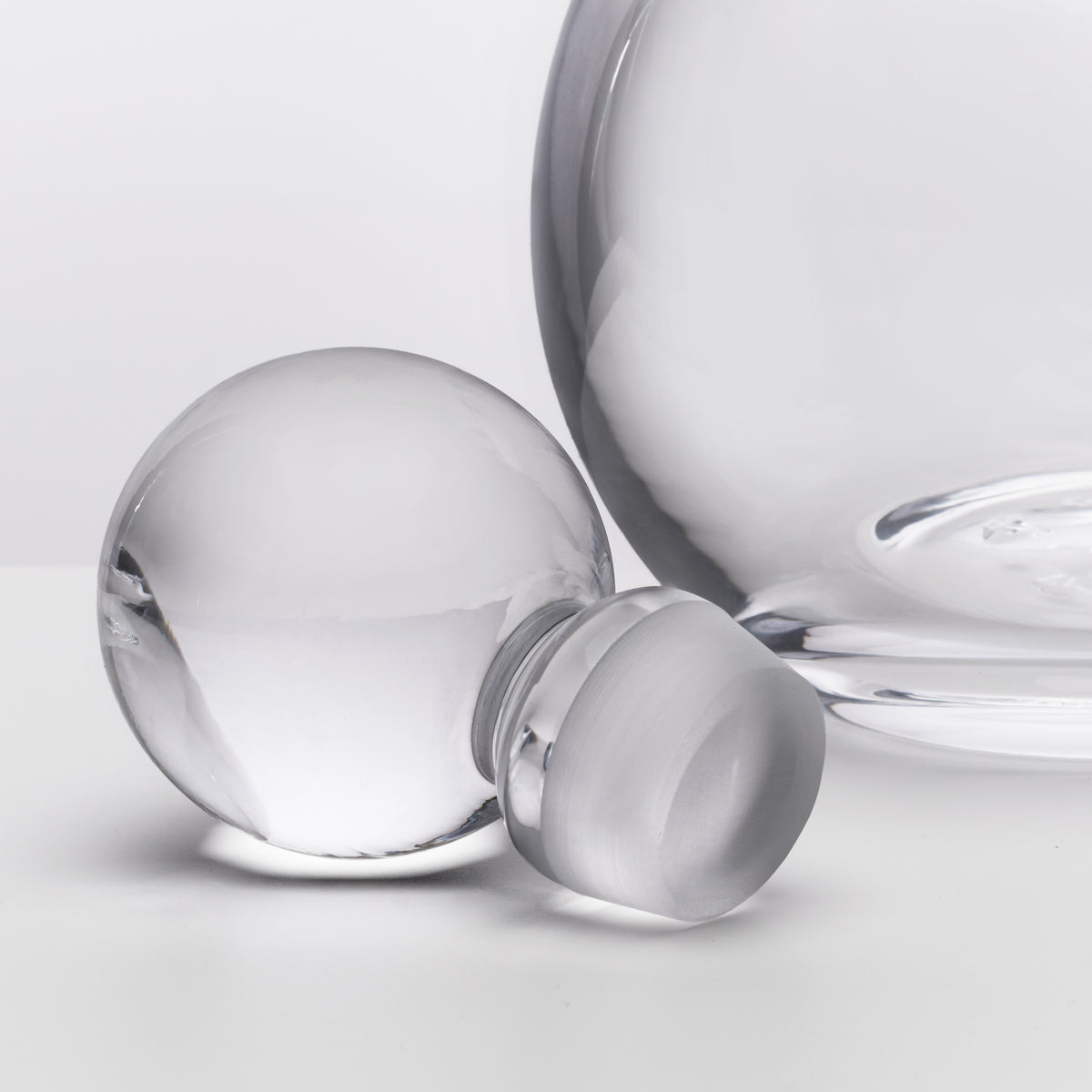 Clear glass decanter with spherical body, curved spout, and matching stopper displayed against white background.