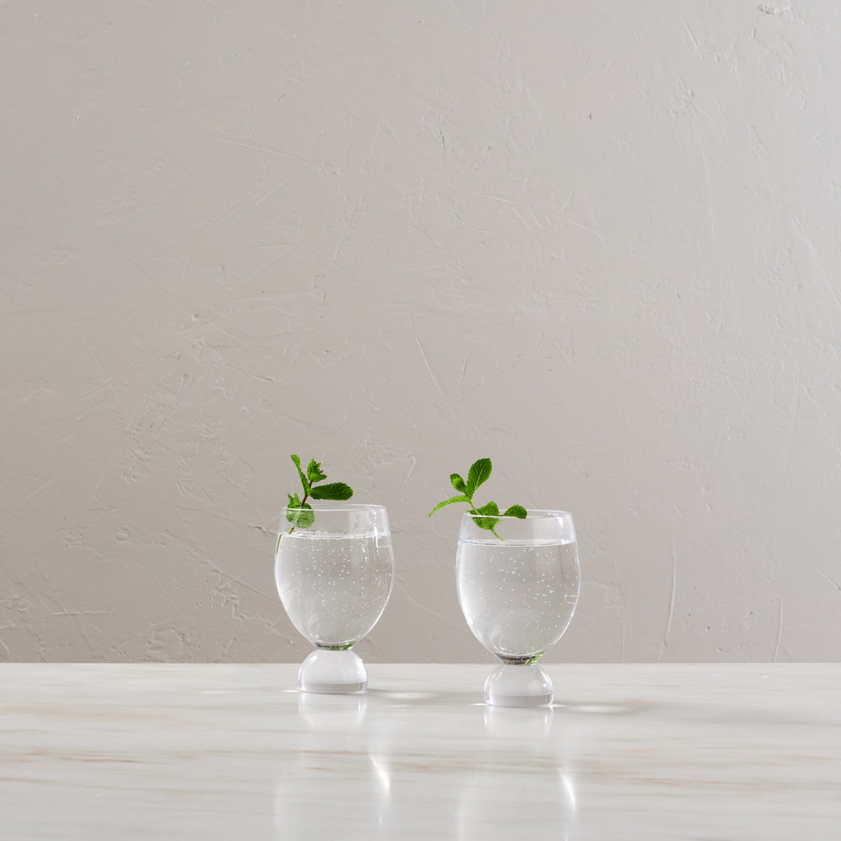 Two clear glass tumblers with white pedestal bases filled with water and garnished with mint sprigs.