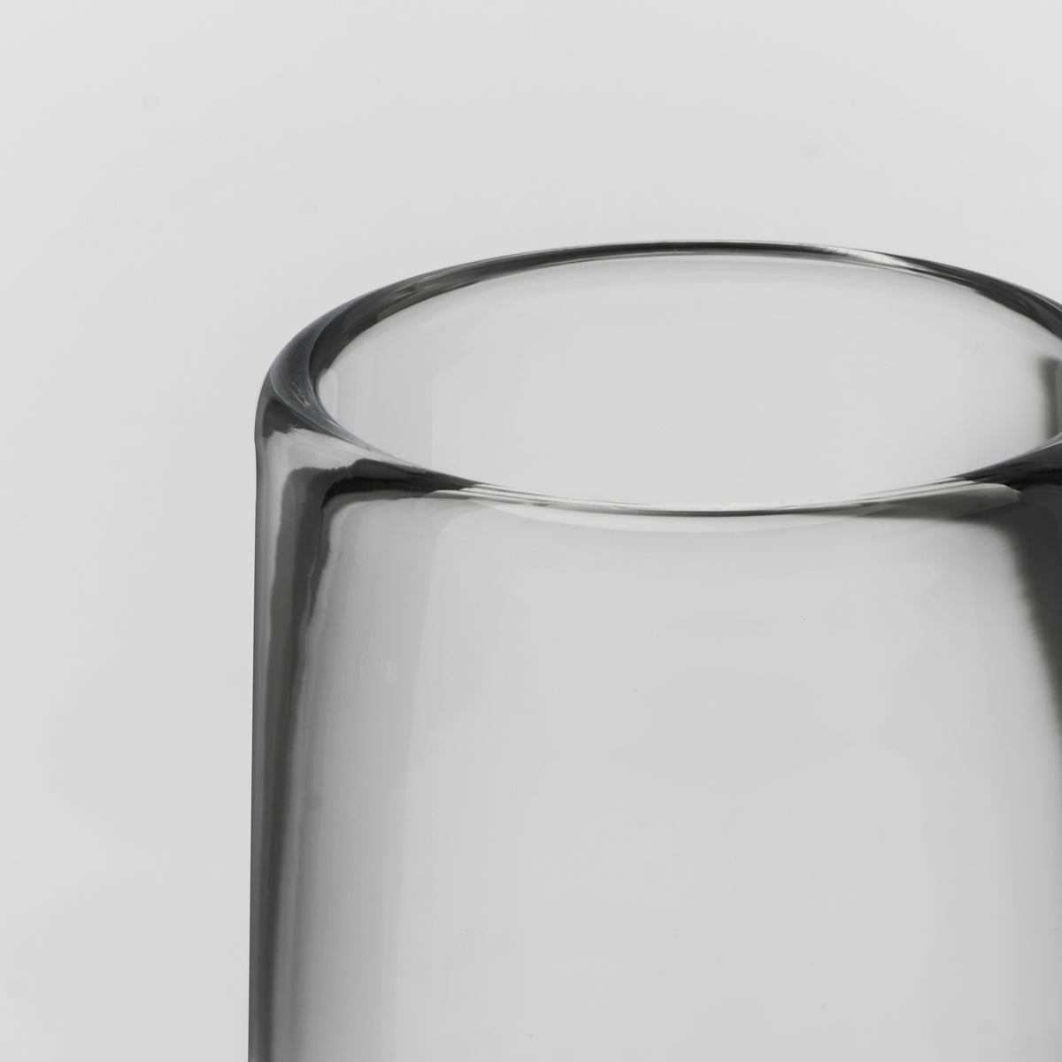 Close-up of a clear glass tumbler or vase showing the top rim and part of the transparent body against a light gray background.