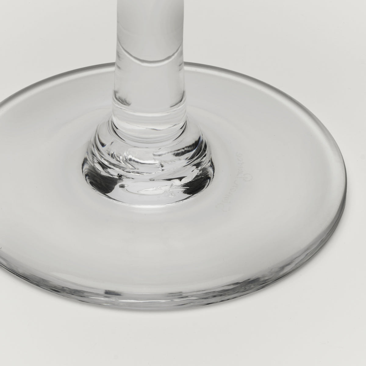 Close-up of a clear glass wine glass base and stem on a light gray background.