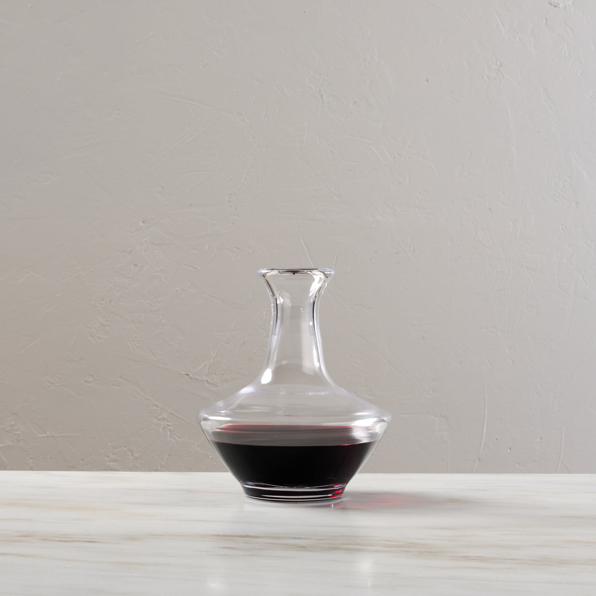 Clear glass wine decanter with wide base and narrow neck, partially filled with red wine.