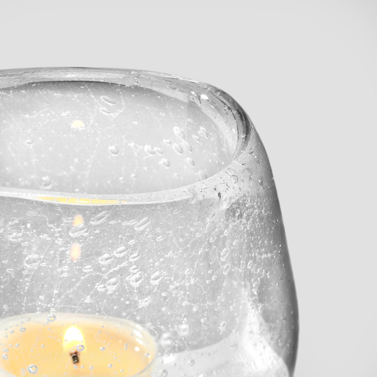 Clear glass tealight holder with textured surface and yellow tealight candle burning inside.