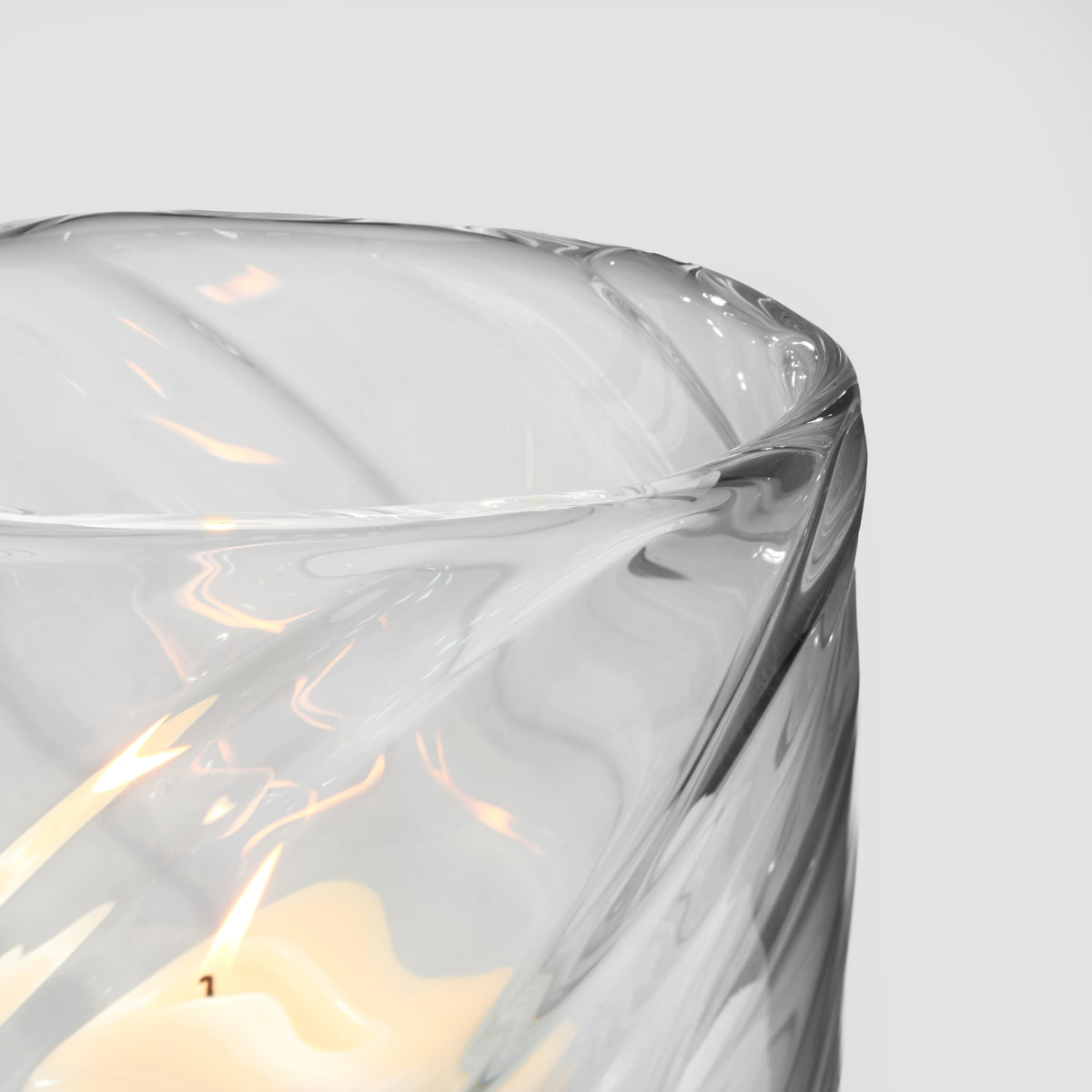Clear glass candle holder with cream-colored wax and swirled gray and white pattern design.
