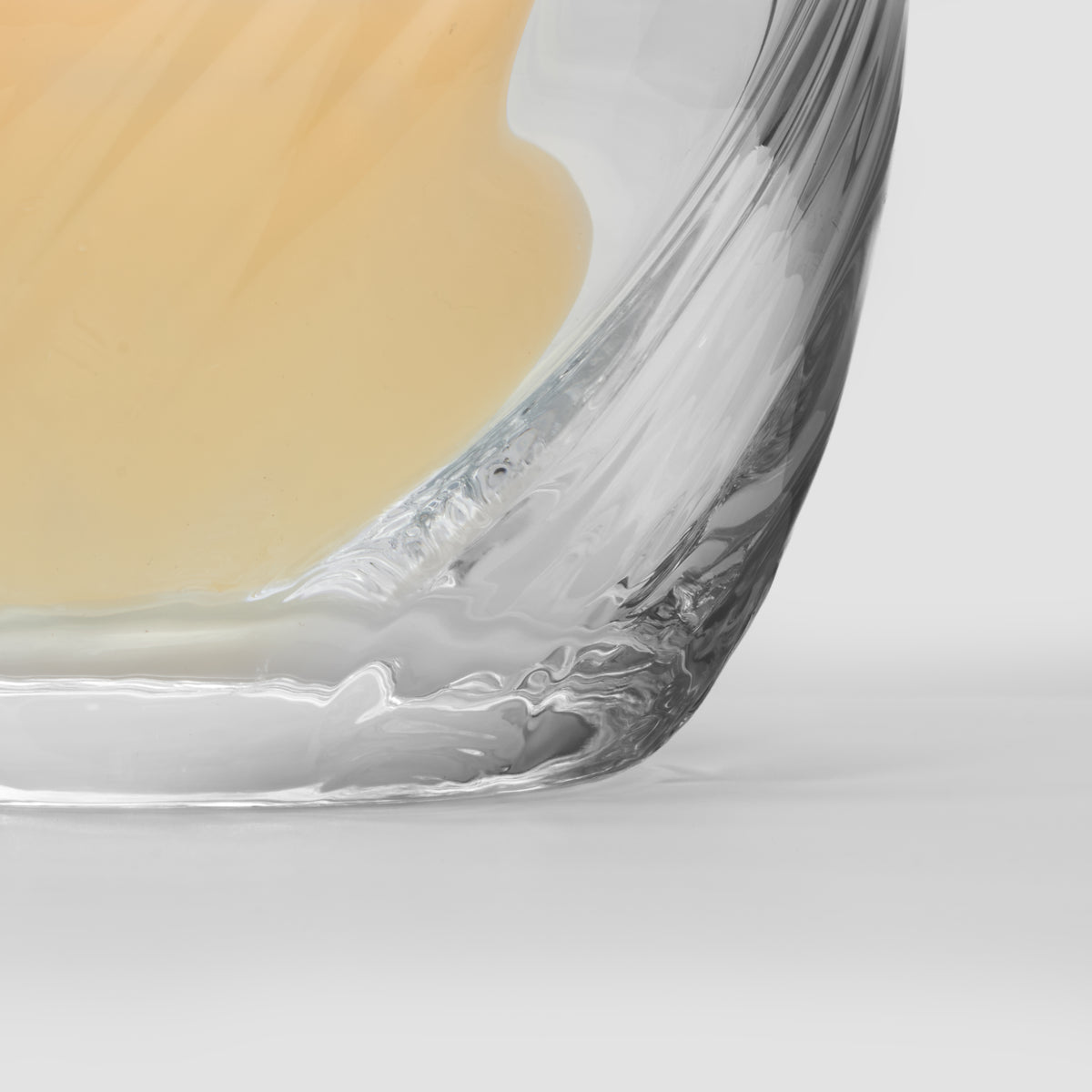 Clear glass bowl with ornate curved rim detail containing pale yellow liquid.