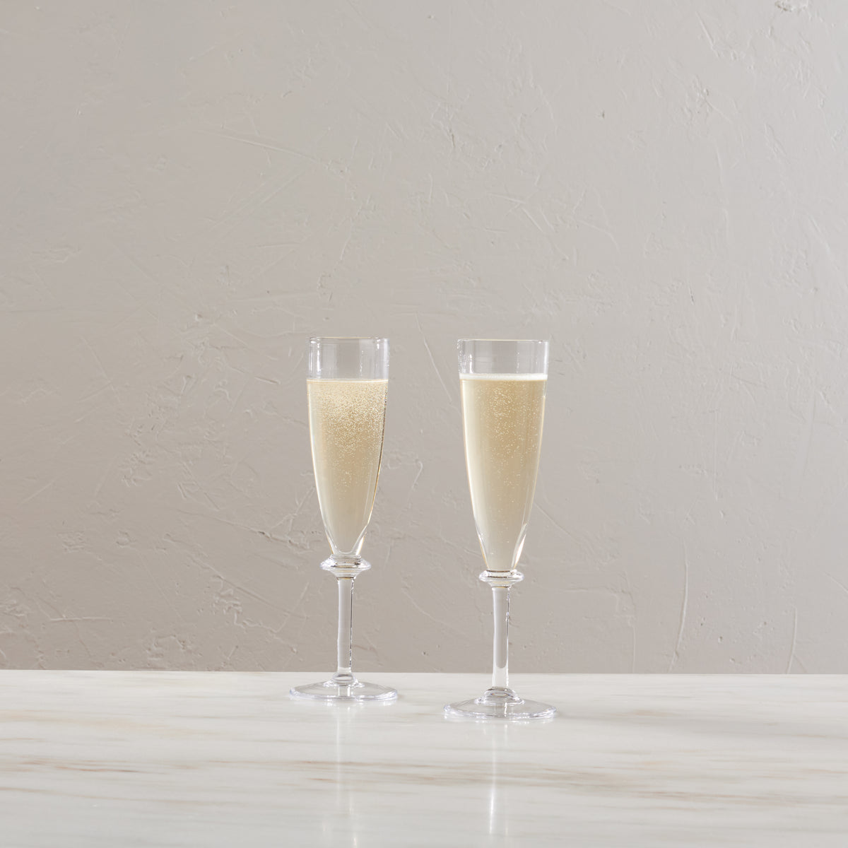 Two clear champagne flutes filled with sparkling wine on a white surface.