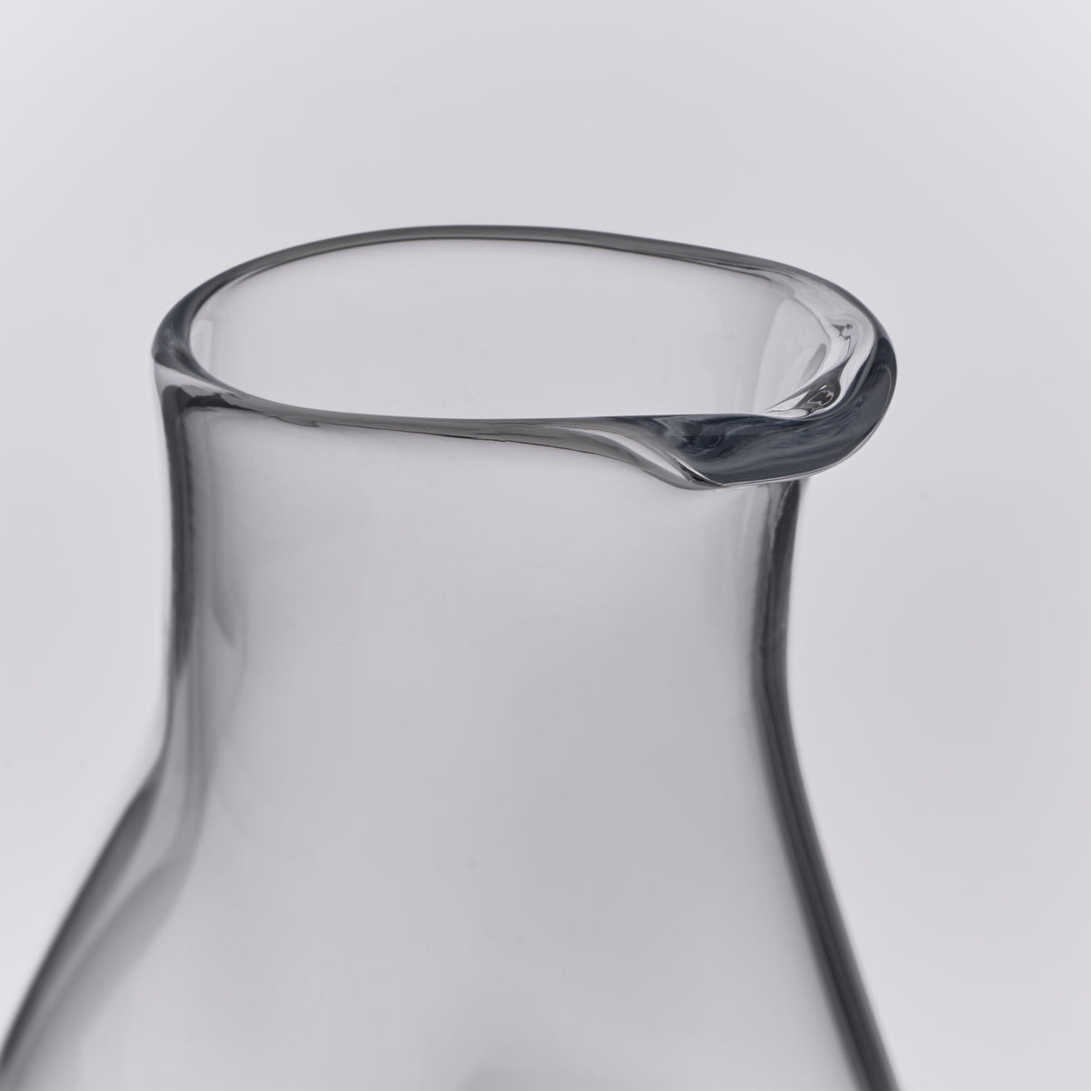 Clear glass carafe with curved sides and a pouring spout at the rim.