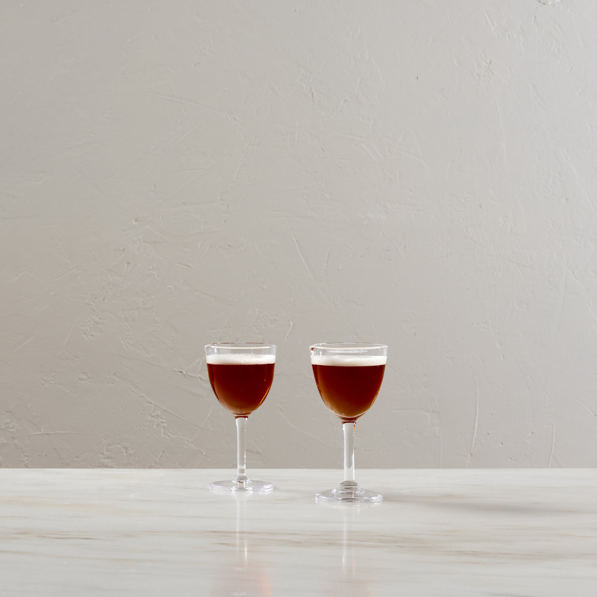 Two clear Nick & Nora glasses filled with red liquid, displayed side by side on a white surface.