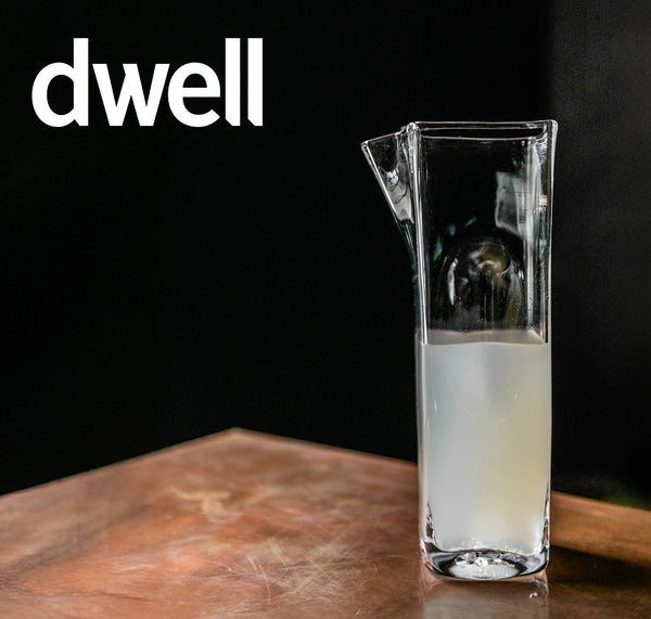 Dwell magazine feature: Simon Pearce handblown glass pitcher with angled lip, filled with a milky white liquid, on a worn copper surface against a dark background
