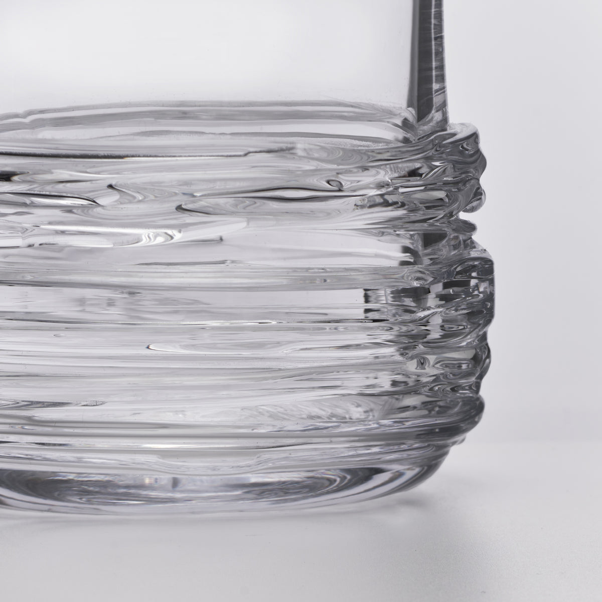 Clear glass decanter with wavy textured body and a tall dark stem on white background.