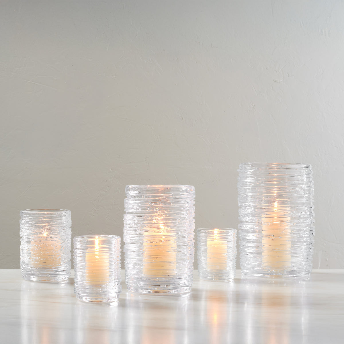 Five clear glass hurricane candles with textured surfaces and lit flames in varying heights arranged in a group.