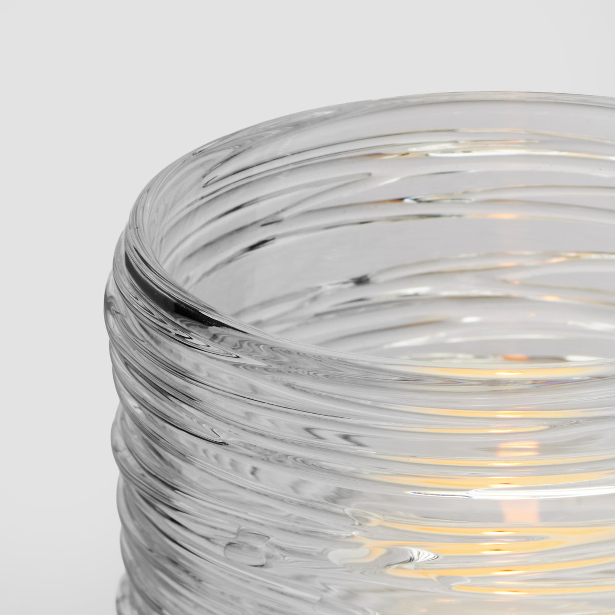 Clear glass tealight holder with horizontal ridged texture and lit candle inside.